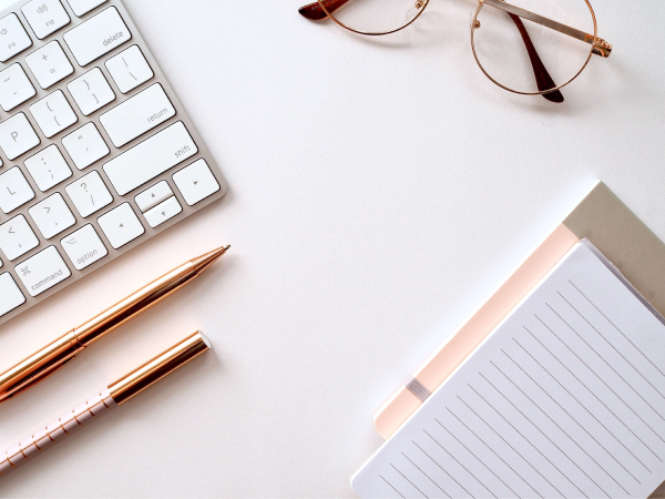 desk with a keyboard, pens, glasses and notebook